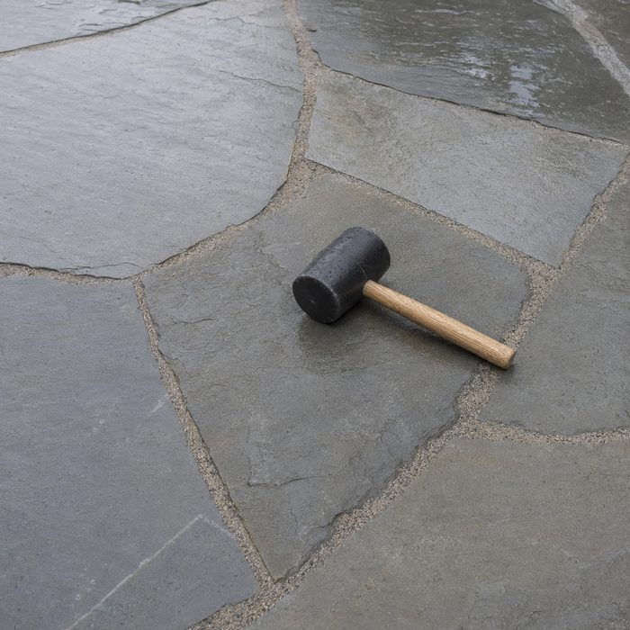 Newly laid grey flagstone with sand swept into the joints and a rubber mallet resting on the stone.