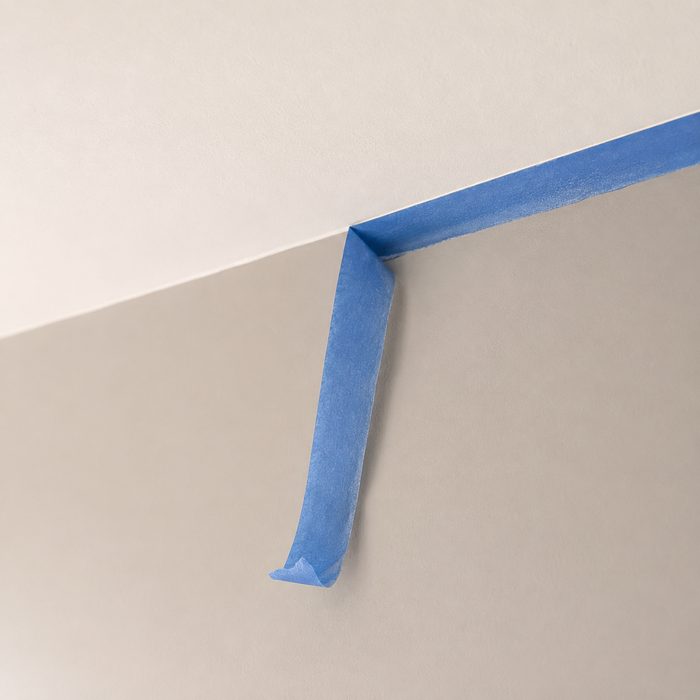 A clean paint line where a wall meets a white ceiling, with blue masking tape half peeled away.