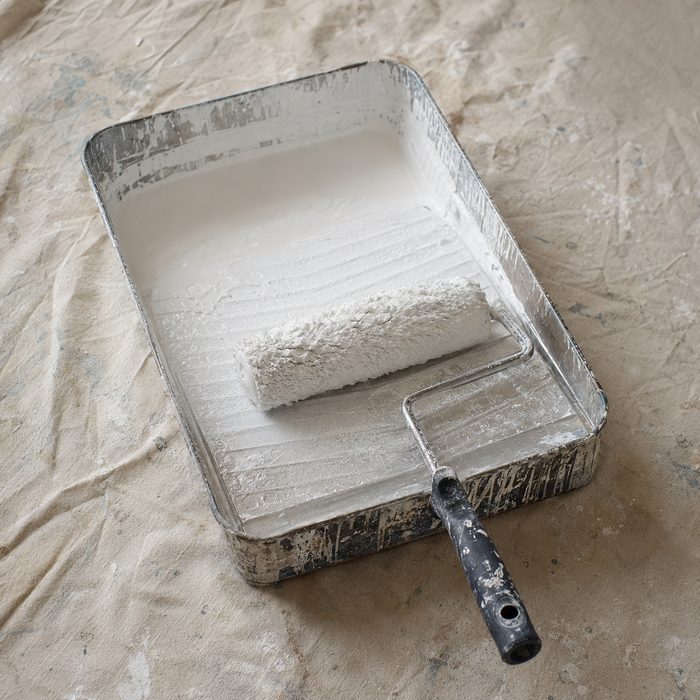 A loaded paint roller resting in a metal tray on a canvas dust sheet.