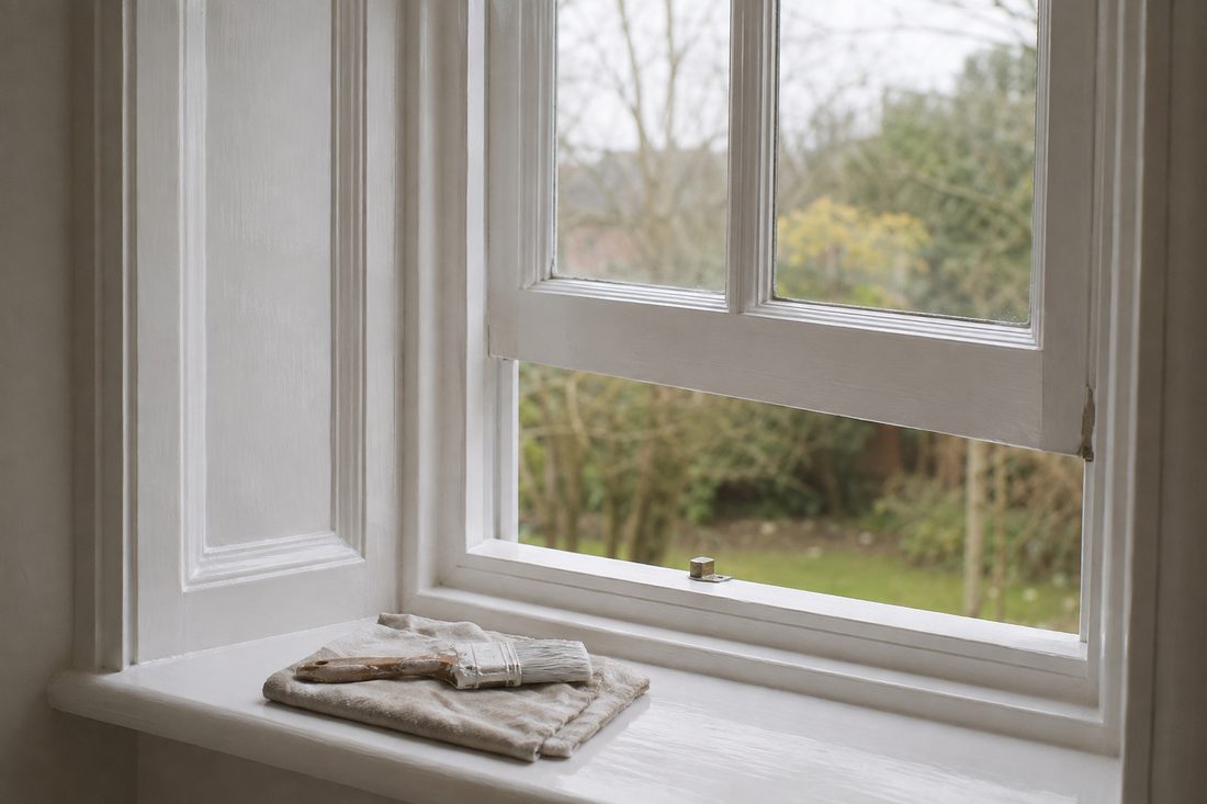 A wooden sash window freshly painted in gloss white, pushed open, with a brush resting on the sill.