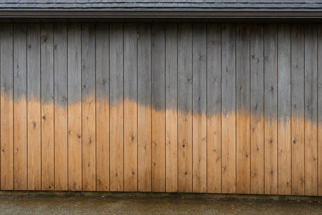 Cedar siding halfway through a soft wash, pale fresh boards below and weathered grey above.